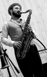 Nil Mujal tocando el saxofón con sombrero y chaleco, en blanco y negro.