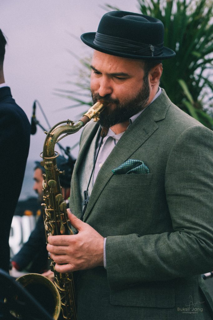 Nil Mujal tocando el saxofón con sombrero y chaqueta gris.